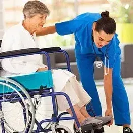 A nurse is helping an elderly woman in a wheelchair.