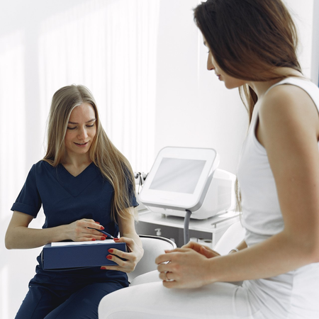 Two women are sitting in front of a machine and talking to each other.