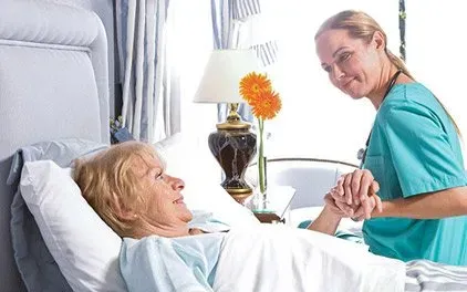 A nurse is holding the hand of an elderly woman in a hospital bed.