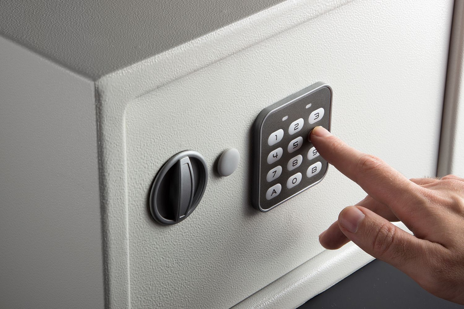 Hand pressing a keypad on a gray wall safe with a round lock Hand pressing a keypad on a gray wall safe with a round lock