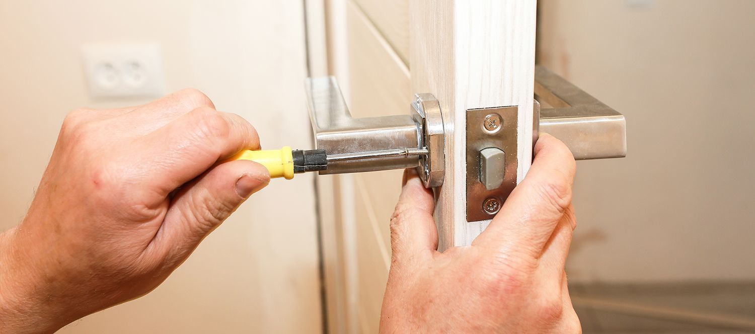 Hands using a screwdriver to tighten a door latch on a white door frame