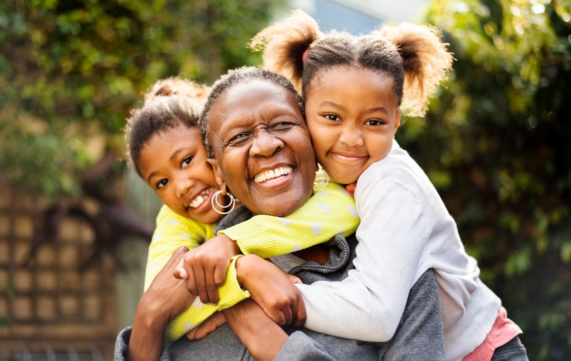 Woman smiling, embraced by two children outdoors.