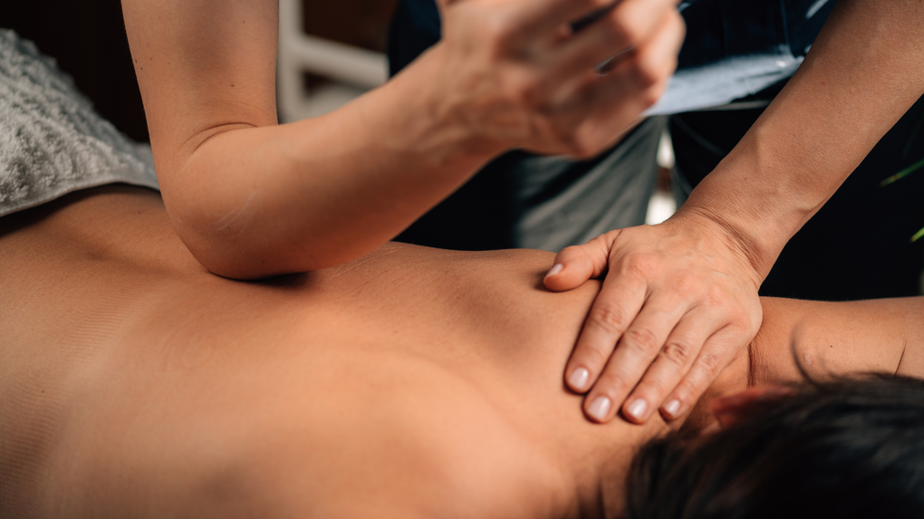 Hands giving a back massage to a person lying face down on a table