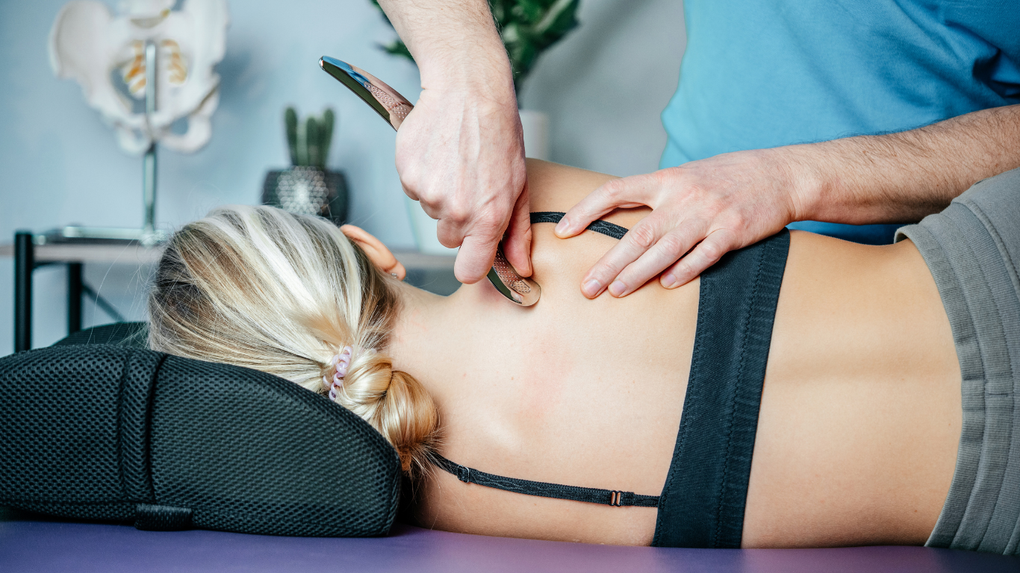 Massage therapist pressing a client's back on a treatment table with a gray towel
