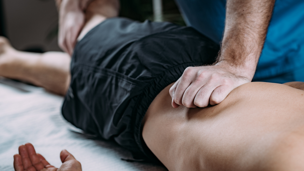 Massage therapist pressing on a person’s lower back on a massage table