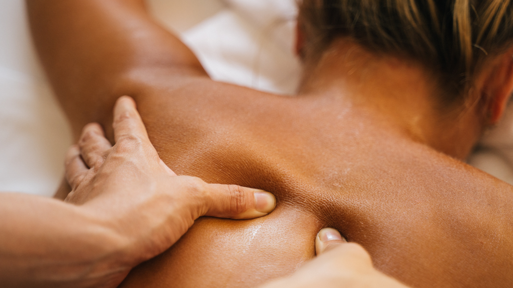 Hands massaging a person's bare upper back in a spa setting
