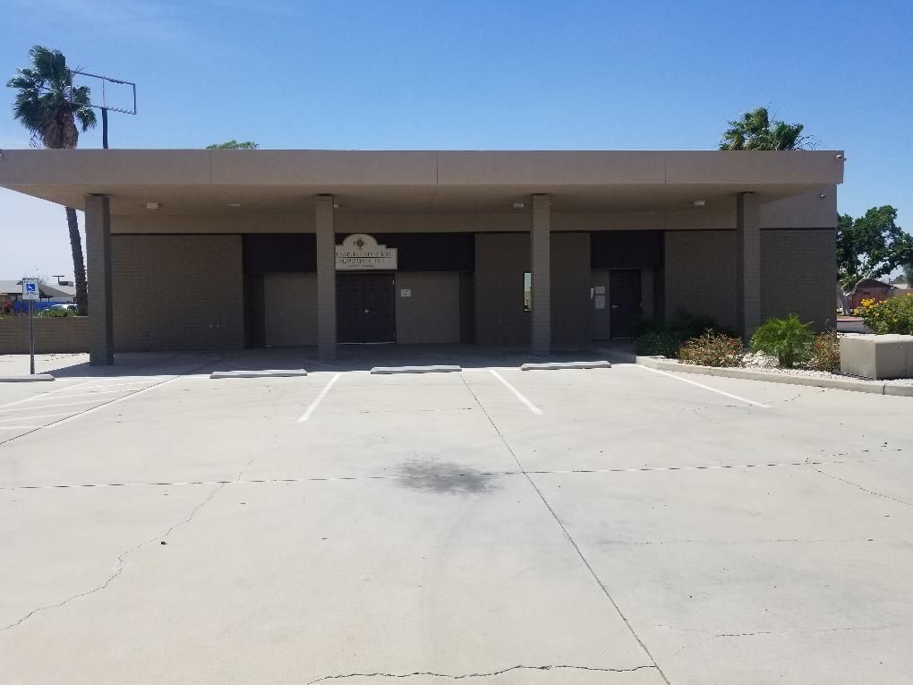 Exterior of a plain gray building with a wide concrete driveway and columns under a flat roof