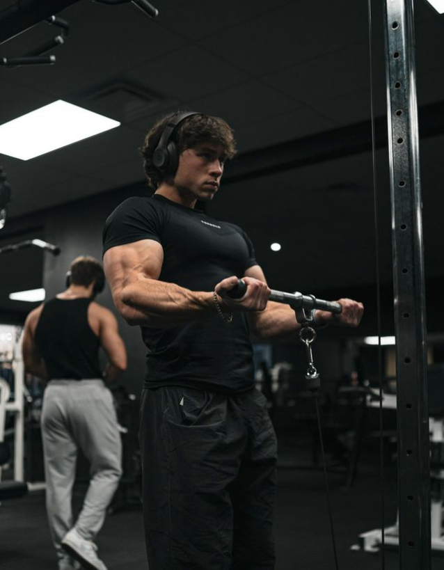 A man wearing headphones is lifting a barbell in a gym.