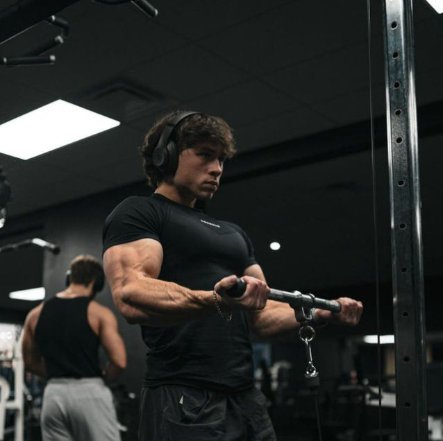 A man wearing headphones is lifting a barbell in a gym