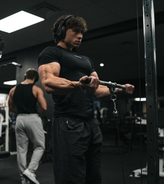 A man wearing headphones is lifting a barbell in a gym.