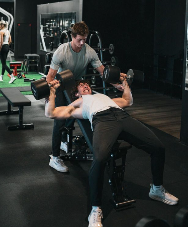 A man is lifting a dumbbell while sitting on a bench in a gym.