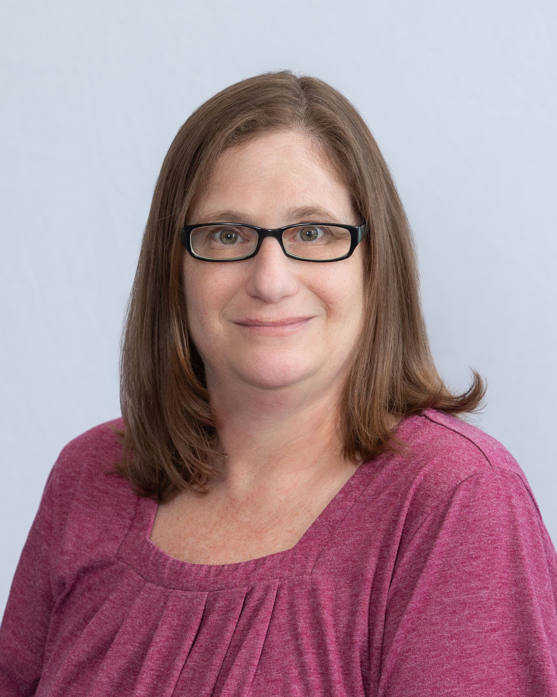 Portrait of a person wearing glasses and a magenta top against a light gray background