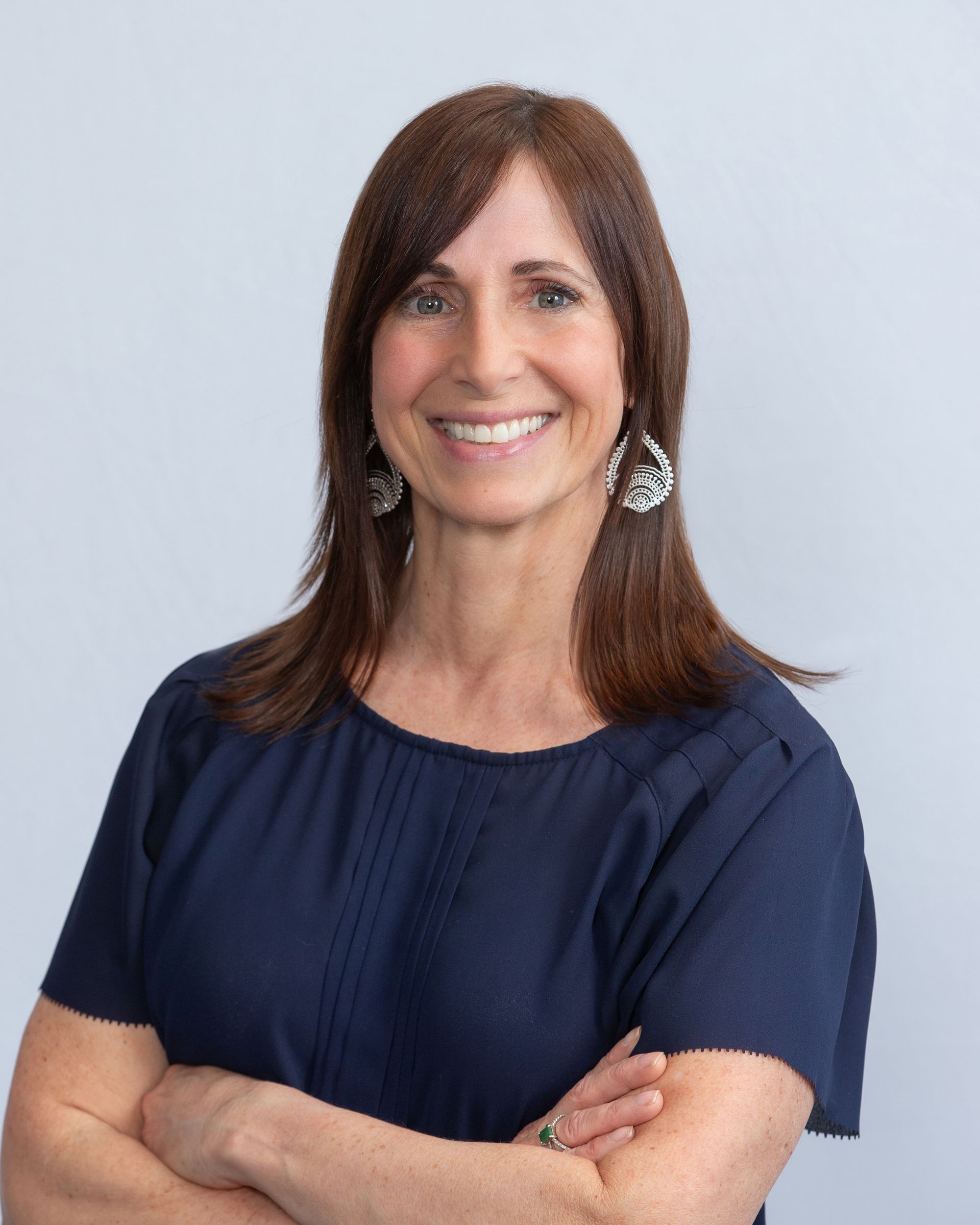 Smiling woman in a navy blue top with arms crossed against a light gray background