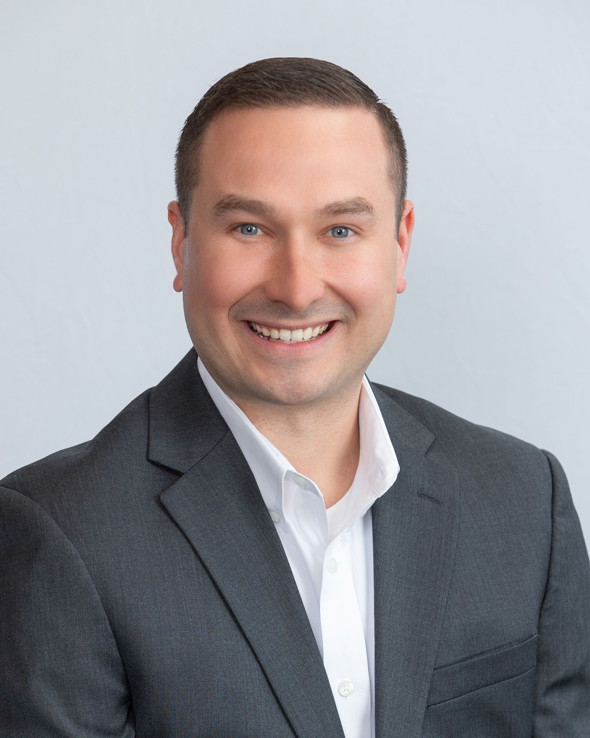 Smiling professional in a gray blazer and white shirt against a light gray background