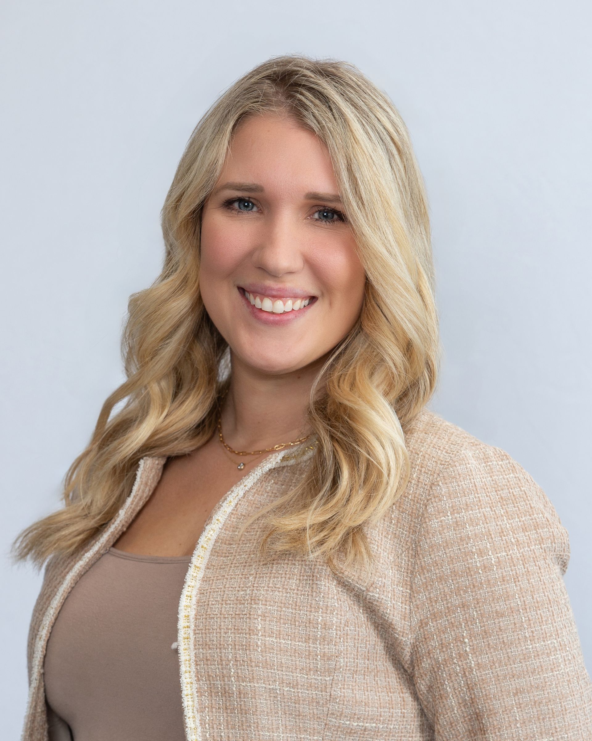 Smiling woman with long blonde hair wearing a beige sweater against a light gray background