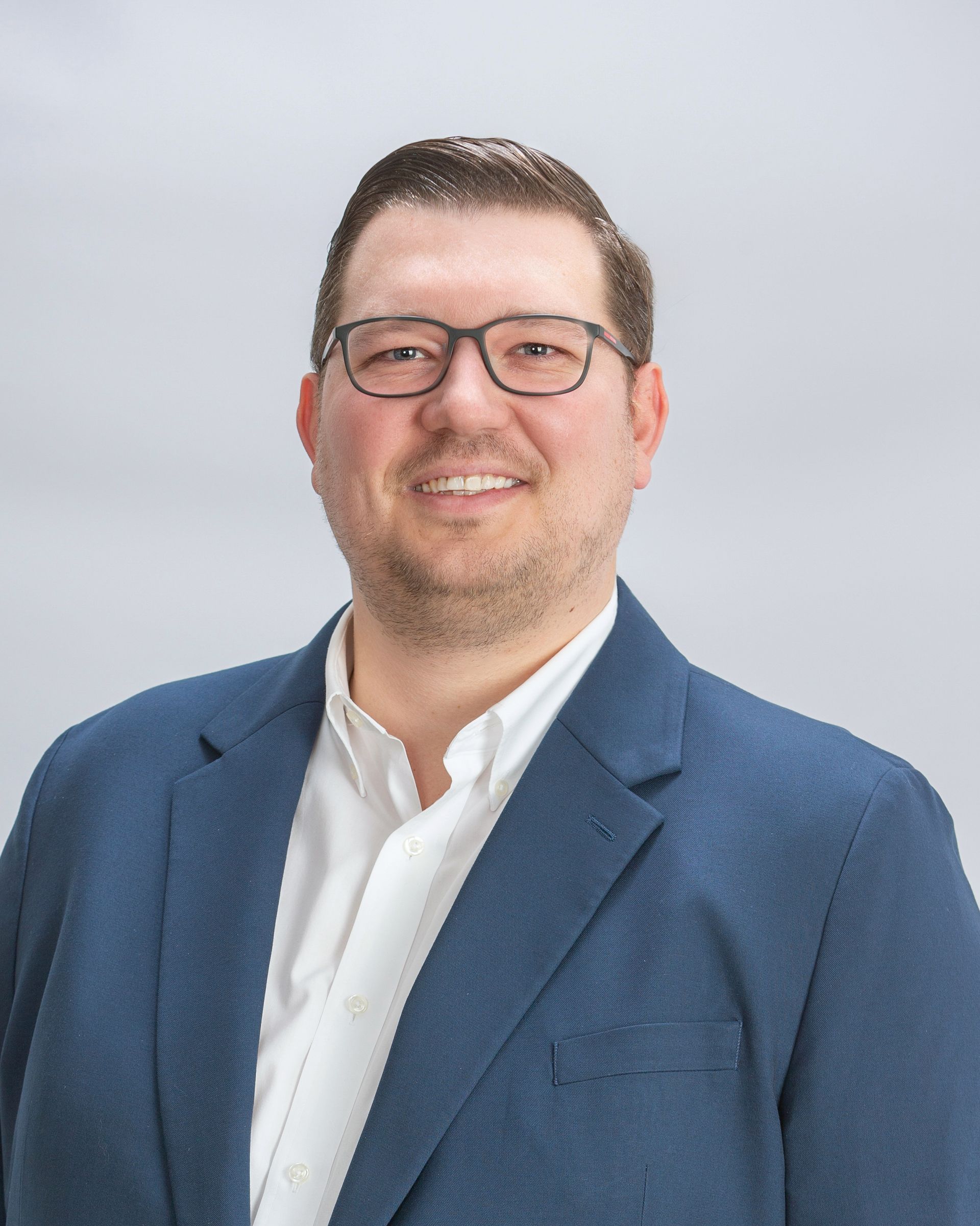 Portrait of a smiling person in glasses wearing a blue blazer and white shirt on a light gray background