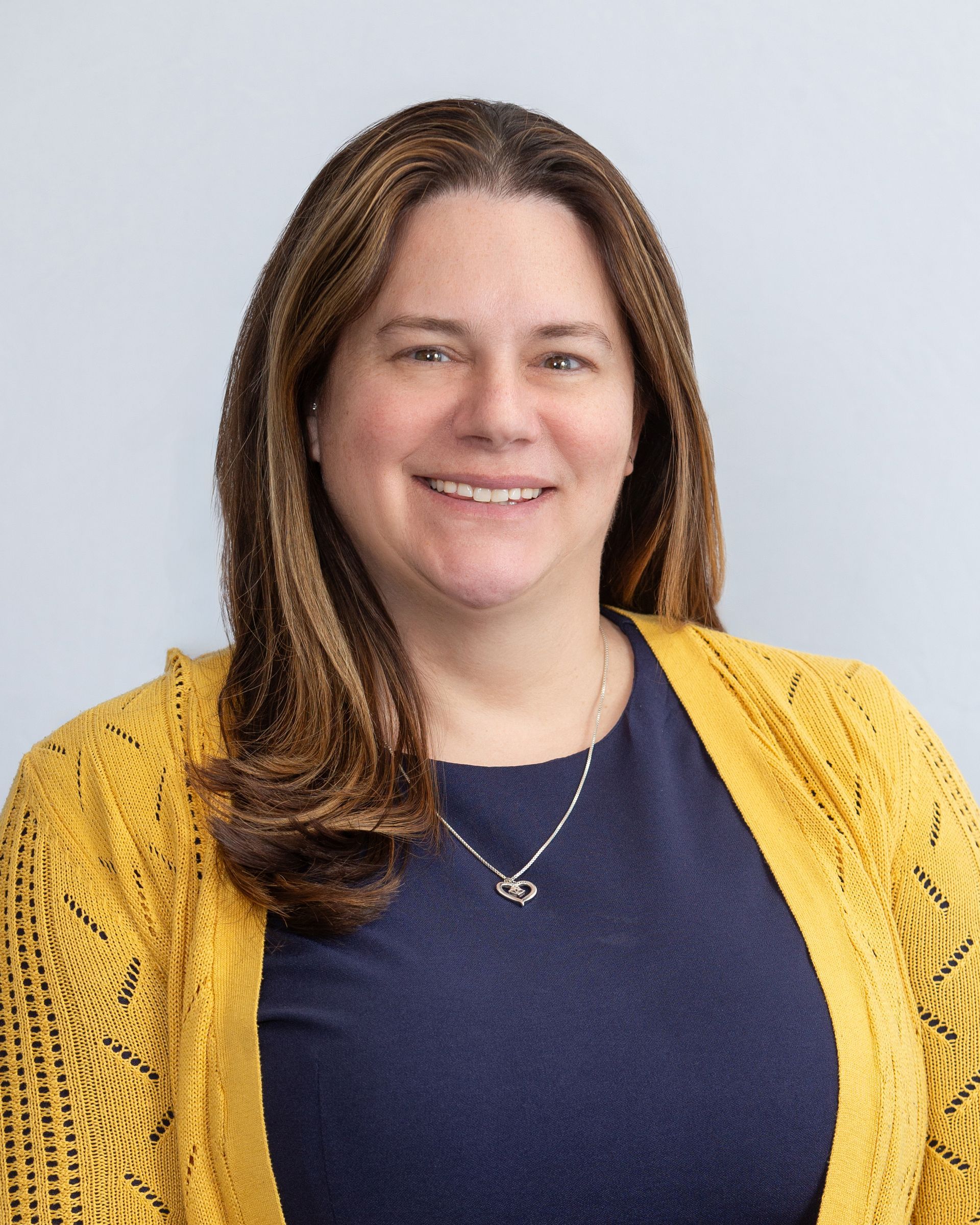 Woman smiling in a navy top and yellow cardigan against a light gray background