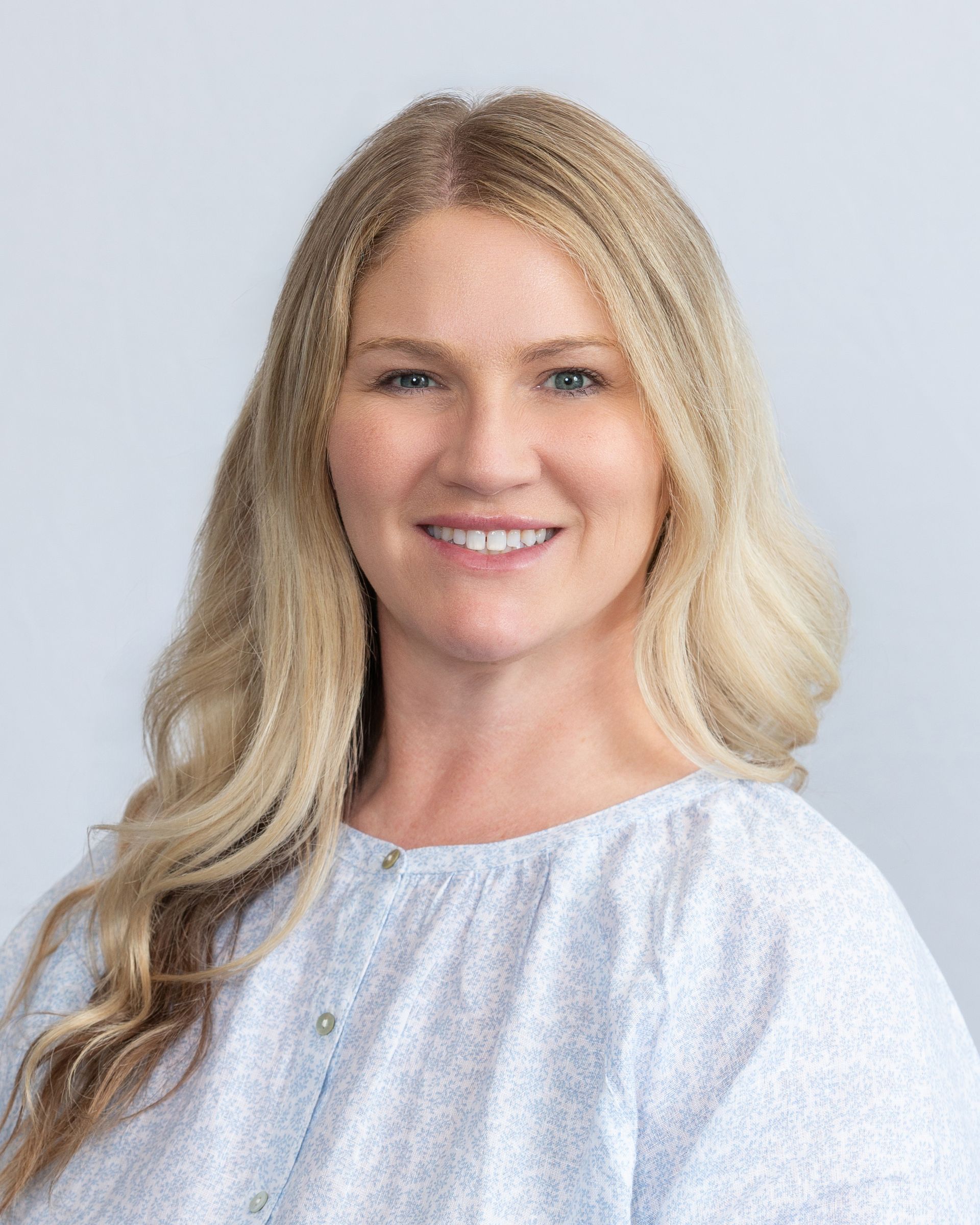 Smiling blonde woman in a light blue blouse against a soft gray background