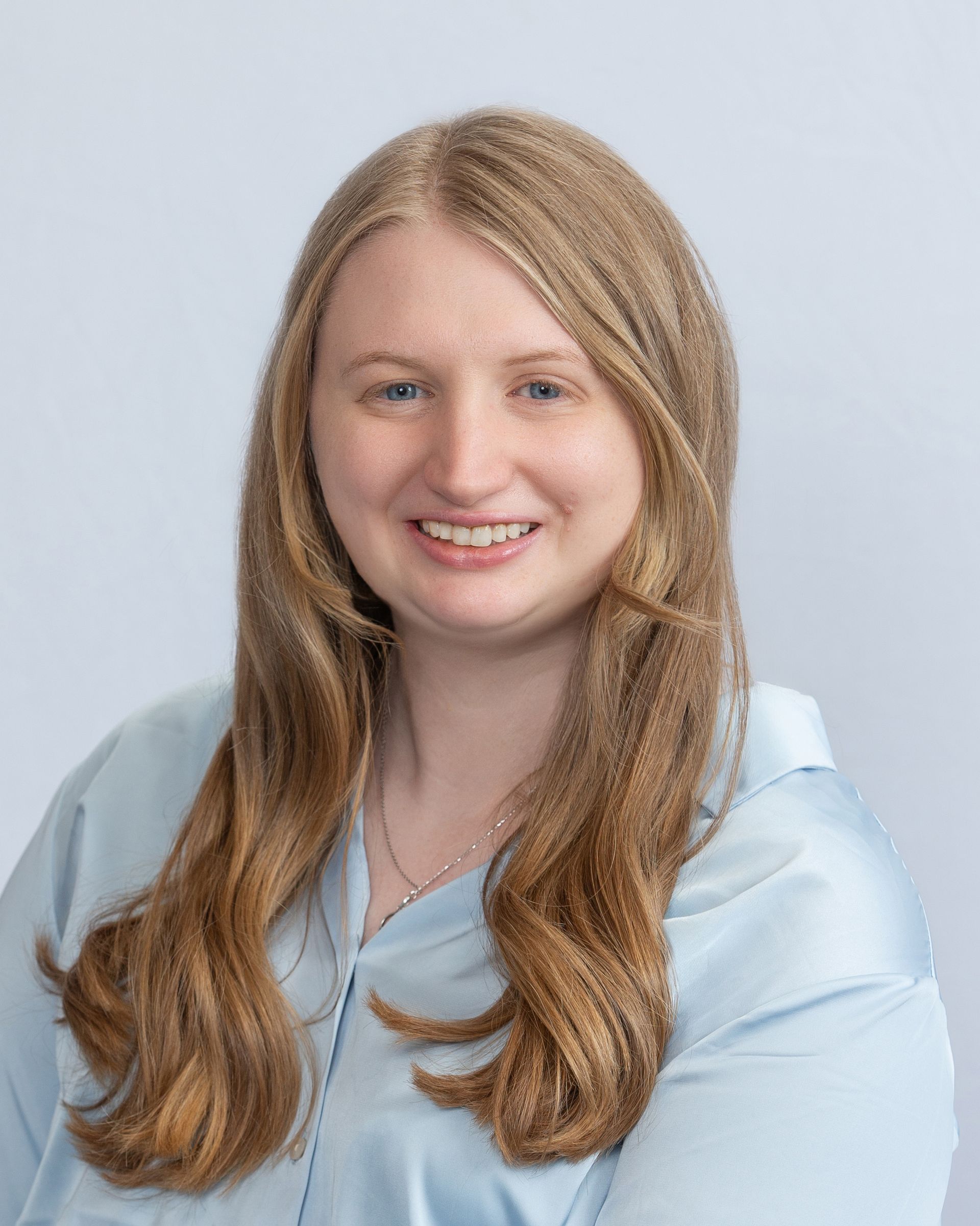 Portrait of a smiling woman in a light blue blouse against a pale gray background