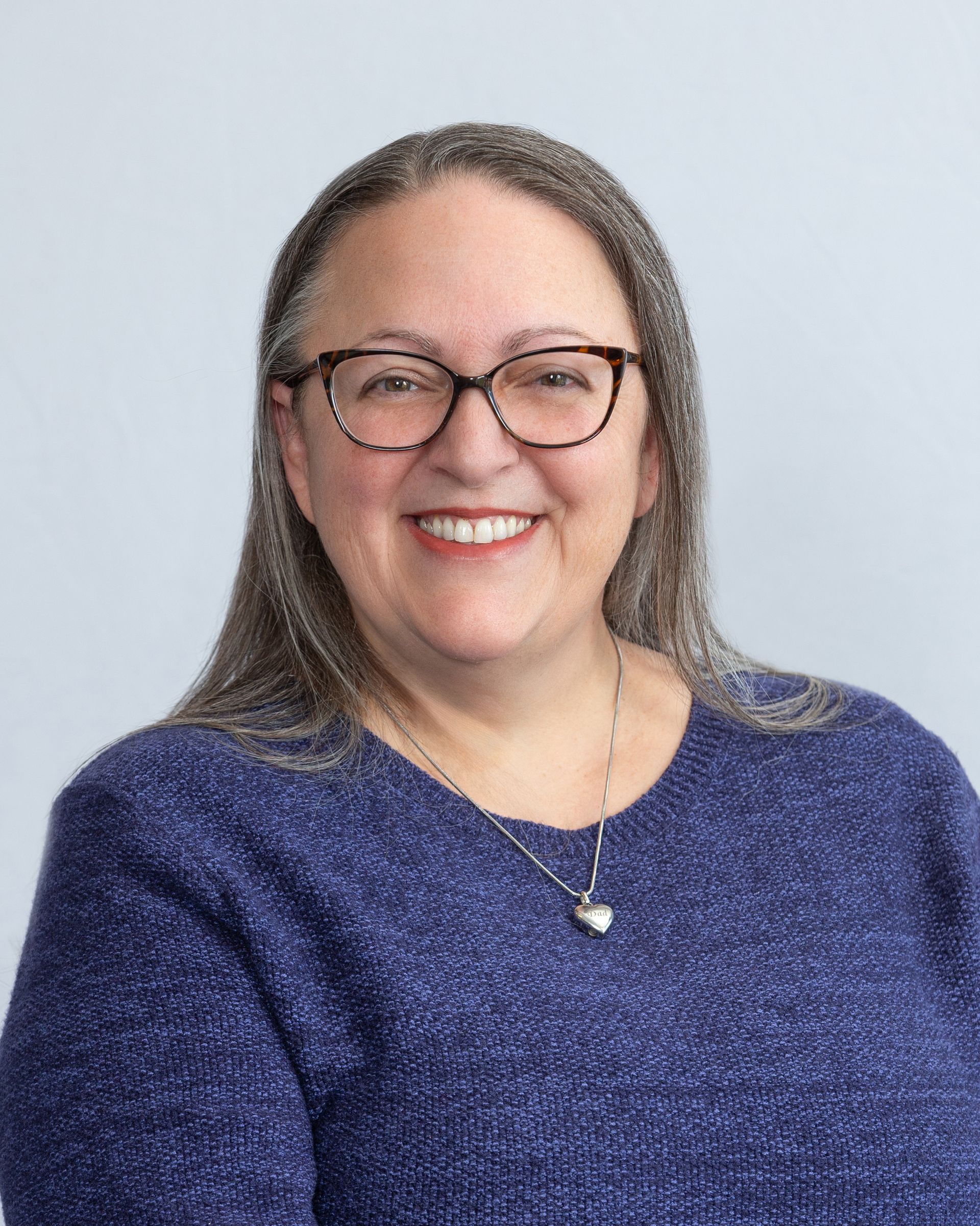 Smiling person with glasses in a blue sweater against a light gray background