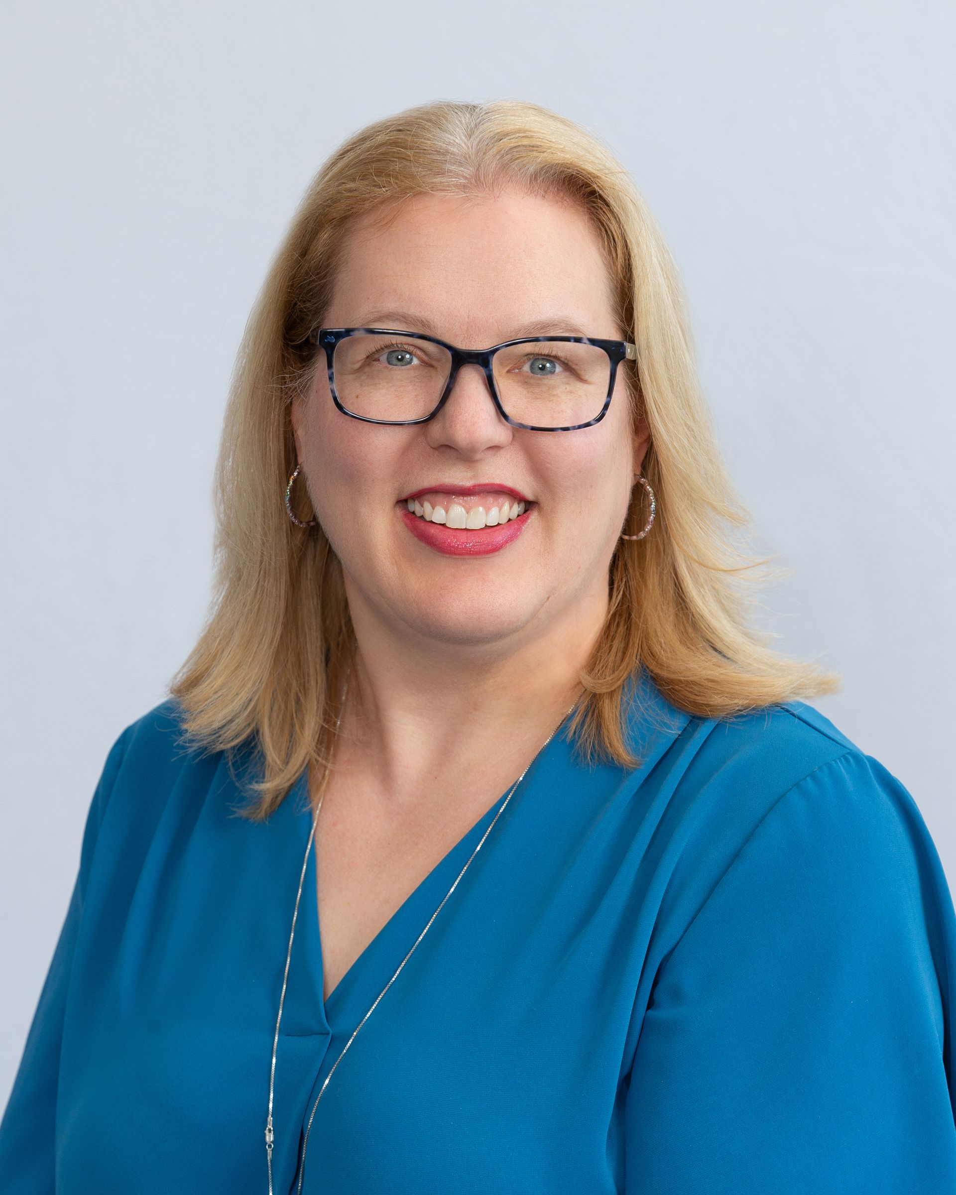 Portrait of a smiling person with glasses in a blue blouse against a light gray background