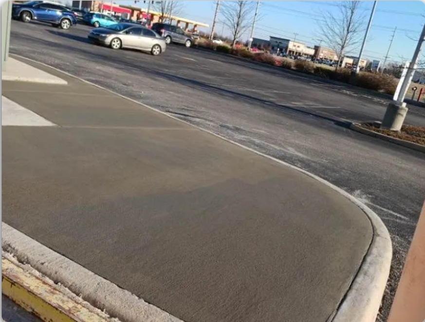 Freshly poured concrete sidewalk beside parking lot with smooth finish at commercial area site.