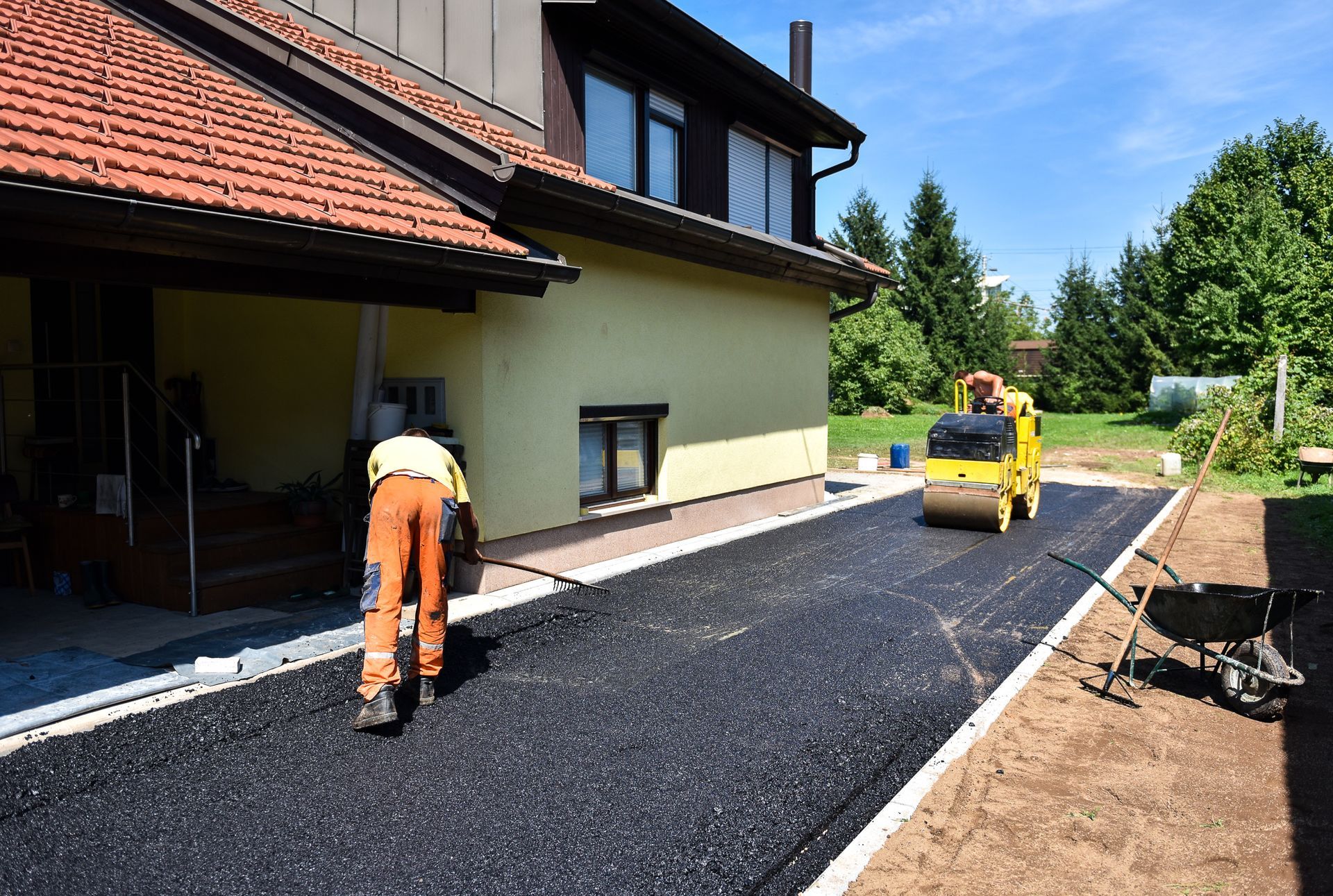 A worker is smoothing fresh asphalt on a driveway beside a house A worker is smoothing fresh asphalt on a driveway beside a house