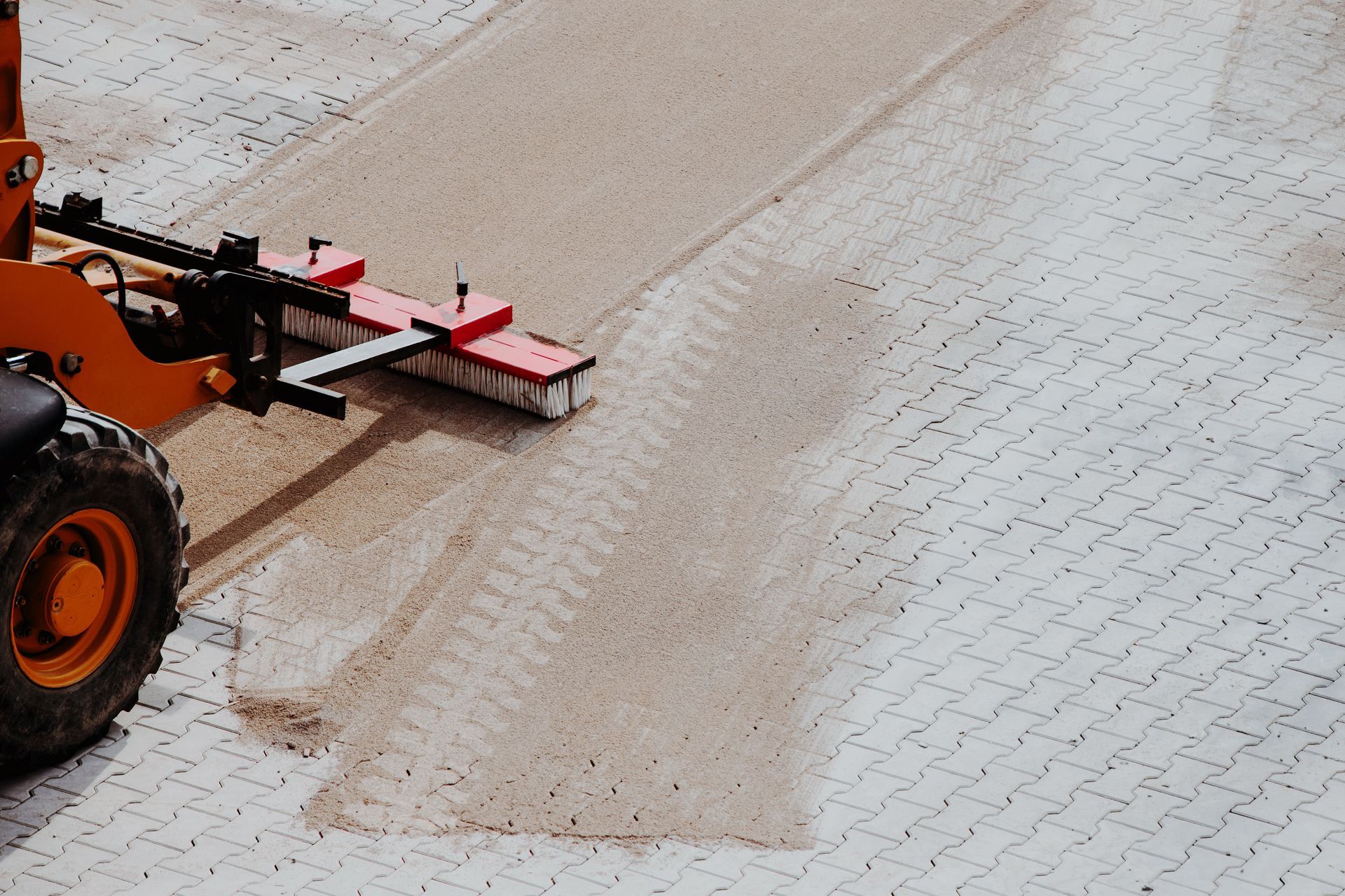 Mechanical broom distributing sand evenly between pavers. Mechanical broom distributing sand evenly between pavers during surface finishing work.