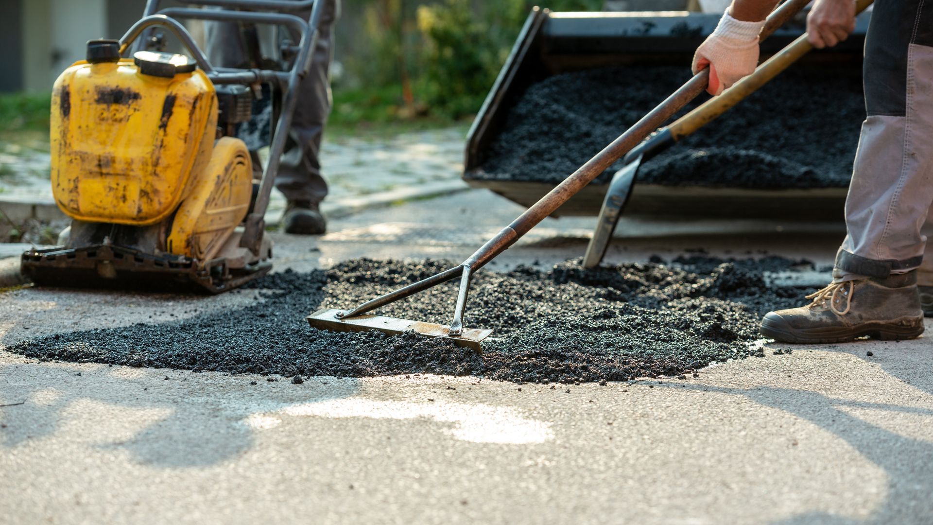 Two workers arranging fresh asphalt mix with rakes and shovels Two workers arranging fresh asphalt mix with rakes and shovels