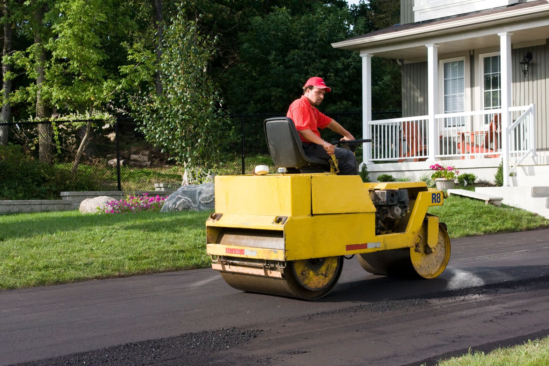 Construction worker smoothing asphalt driveway using a heavy roller machine.