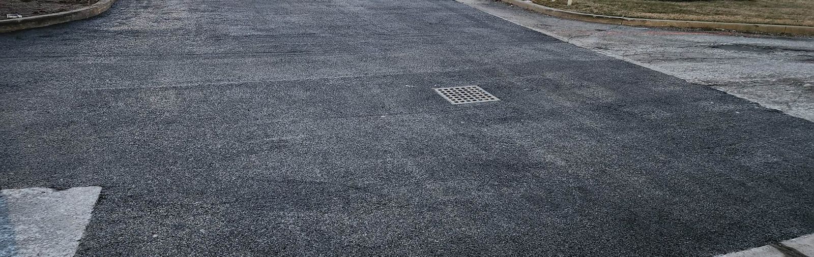 Close-up of a dark gray asphalt road surface with a white line on the side and two recessed metal plates.