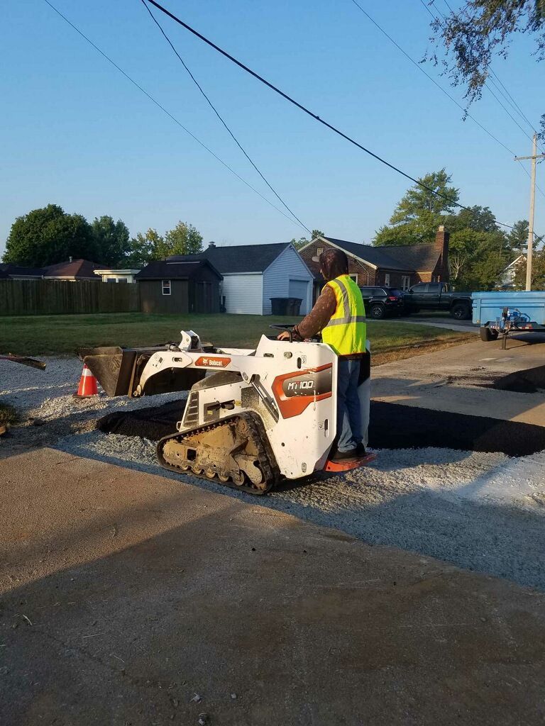 Person operating a white Bobcat skid-steer loader on a gravel surface, wearing a yellow safety vest.