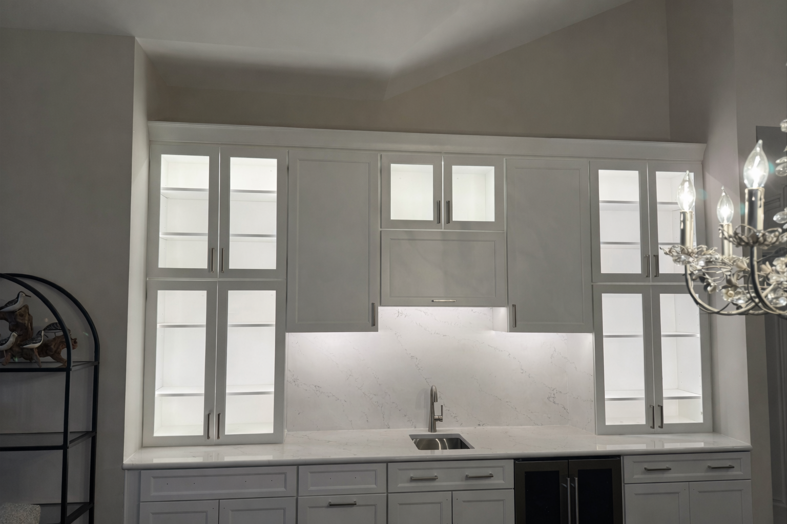 White kitchen cabinets with glass doors, illuminated interior, and a countertop sink.