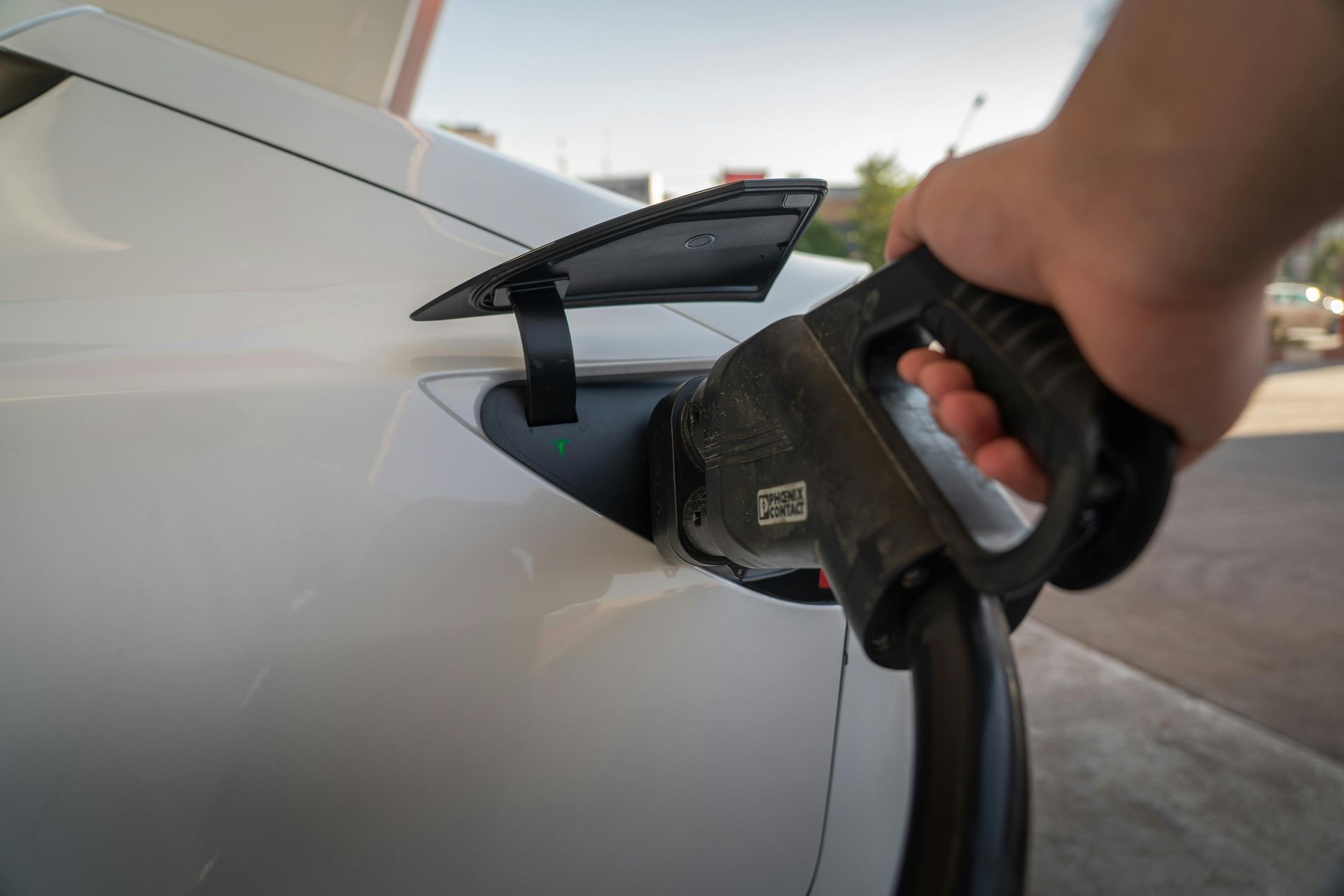 Hand holding a black charging cable inserting into a white electric car.