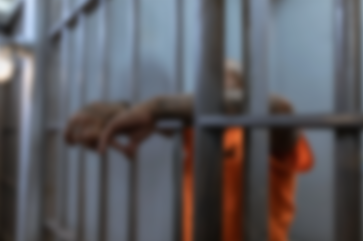 A picture of hands resting on bars of a jail cell.