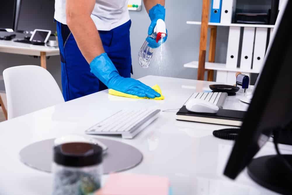 A Man Is Cleaning A Desk In An Office With A Spray Bottle — FNQ Cleaning Services in Mount Sheridan, QLD