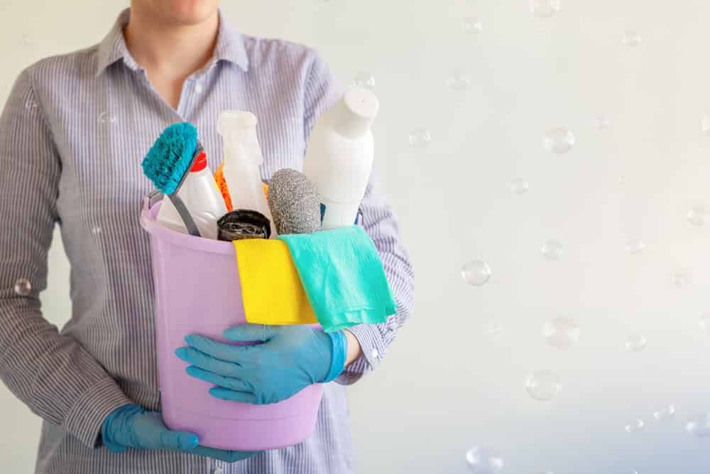 A Woman Is Holding A Bucket Full Of Cleaning Supplies — FNQ Cleaning Services in Mooroobool, QLD