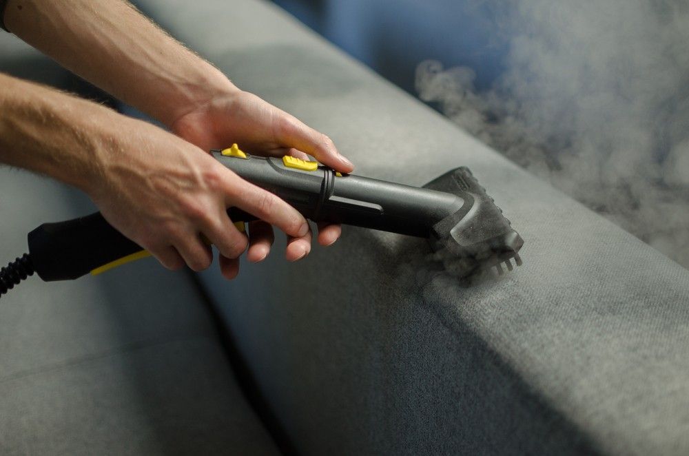 A Person is Cleaning a Couch With a Steam Cleaner — FNQ Cleaning Services in Mooroobool, QLD