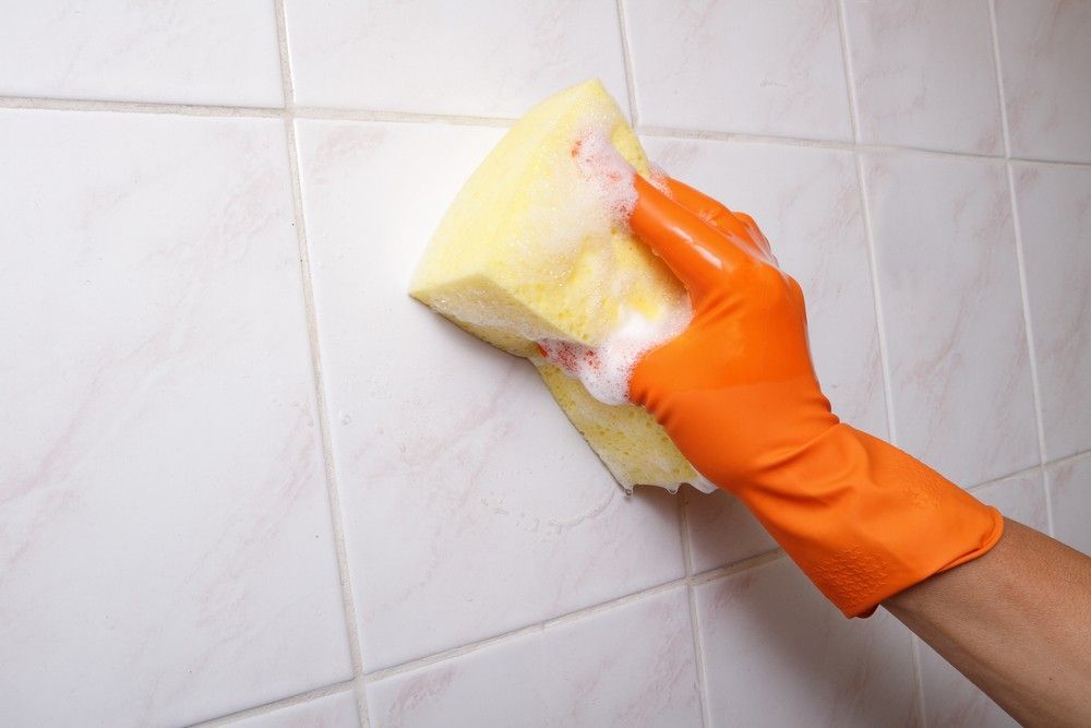 A Person Wearing Orange Gloves is Cleaning a Tile Wall With a Sponge — FNQ Cleaning Services in Mooroobool, QLD