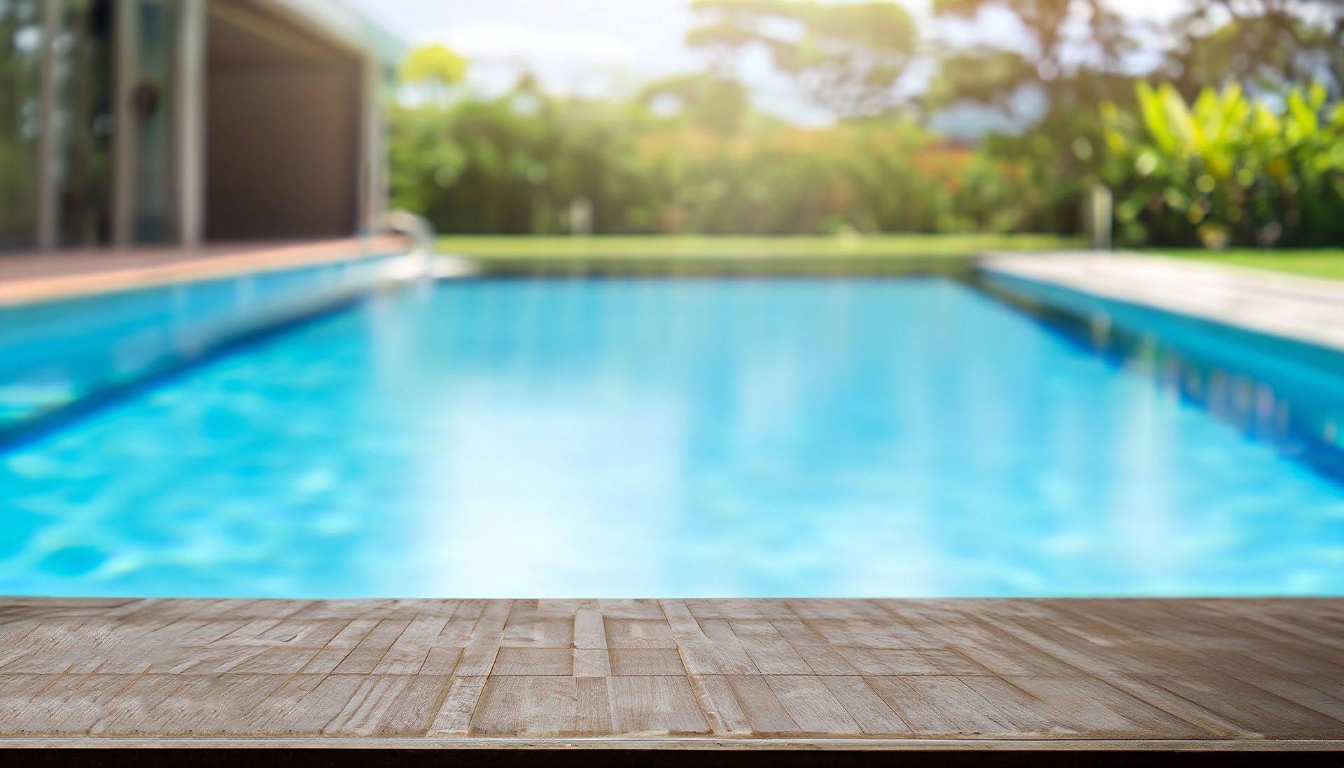 Superficie di legno in primo piano, piscina sullo sfondo, luce solare intensa.
