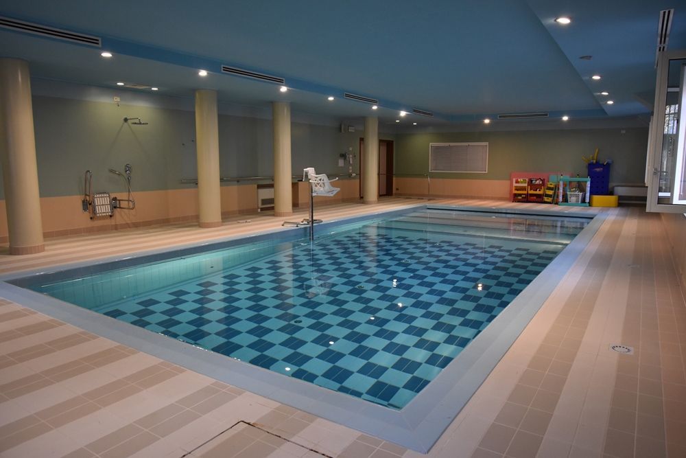 Piscina coperta con piastrelle a scacchi, pavimento beige, soffitto blu e illuminazione da incasso.