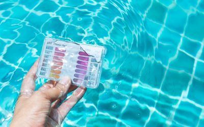 Mano che tiene un kit per il test dell'acqua della piscina davanti a una piscina piastrellata blu.