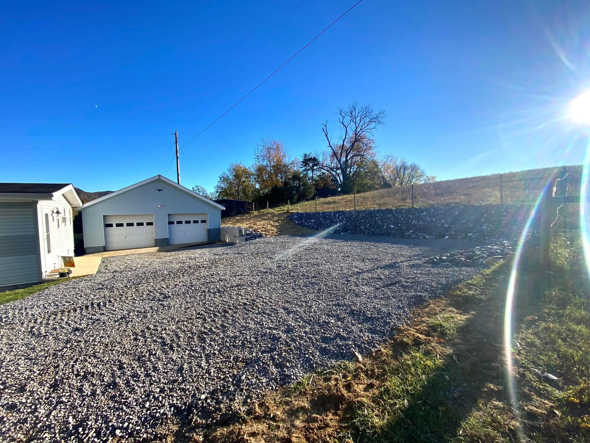 Gravel garage pad, graded and leveled with proper drainage and erosion control installed along perimeter with blue sky.