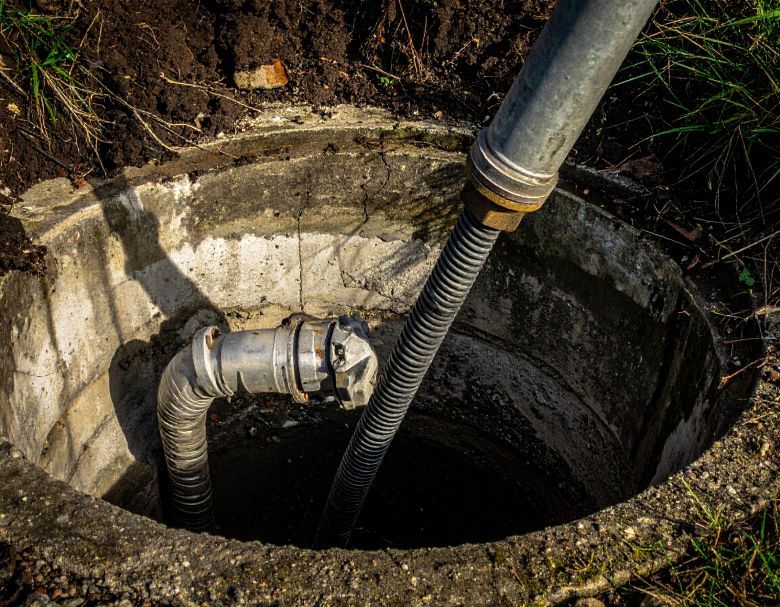Open manhole with pipes and a hose descending into a dark concrete shaft