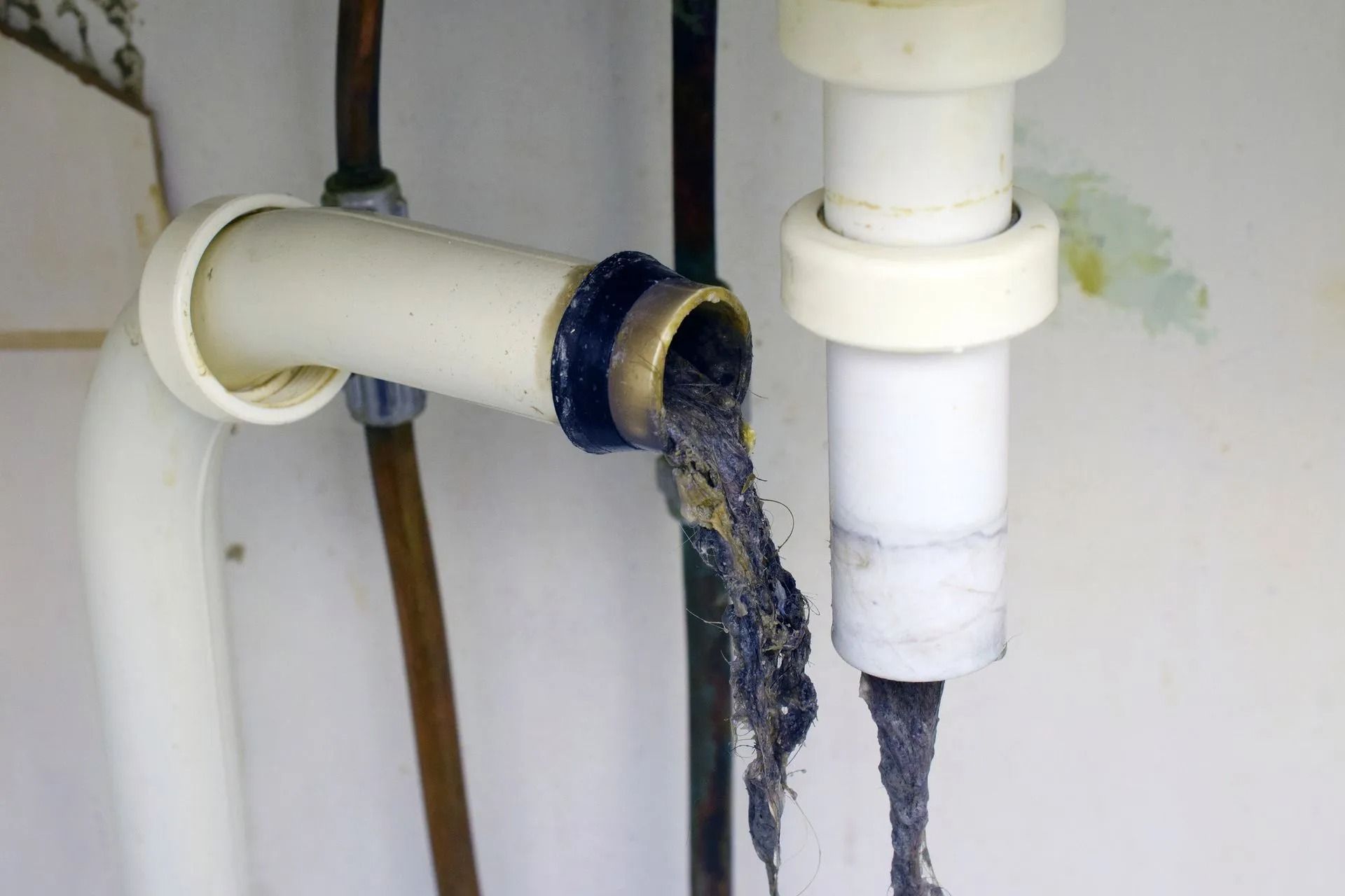 A detached white plumbing pipe revealing a large, dark mass of trapped hair and debris inside.
