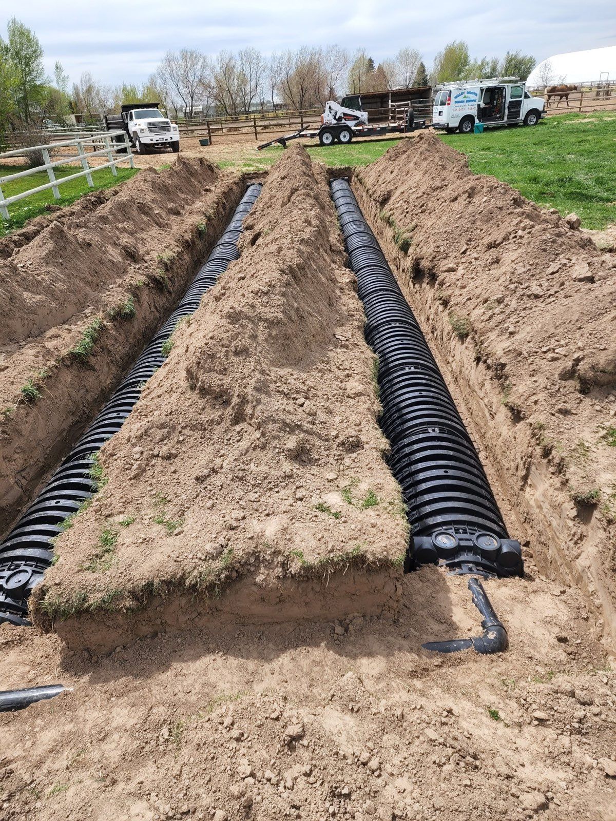 Two parallel rows of black plastic septic drain field chambers installed in trenches in a grassy, rural setting.