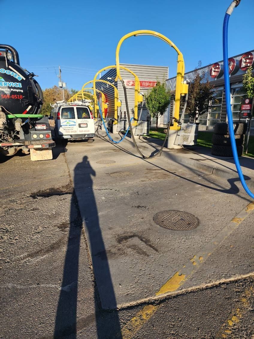 A row of yellow car wash vacuum arches on an asphalt lot, with a service van and tank truck parked nearby.