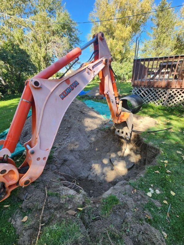 An orange Komatsu backhoe excavator digging a hole in a residential grassy yard near a wooden deck.
