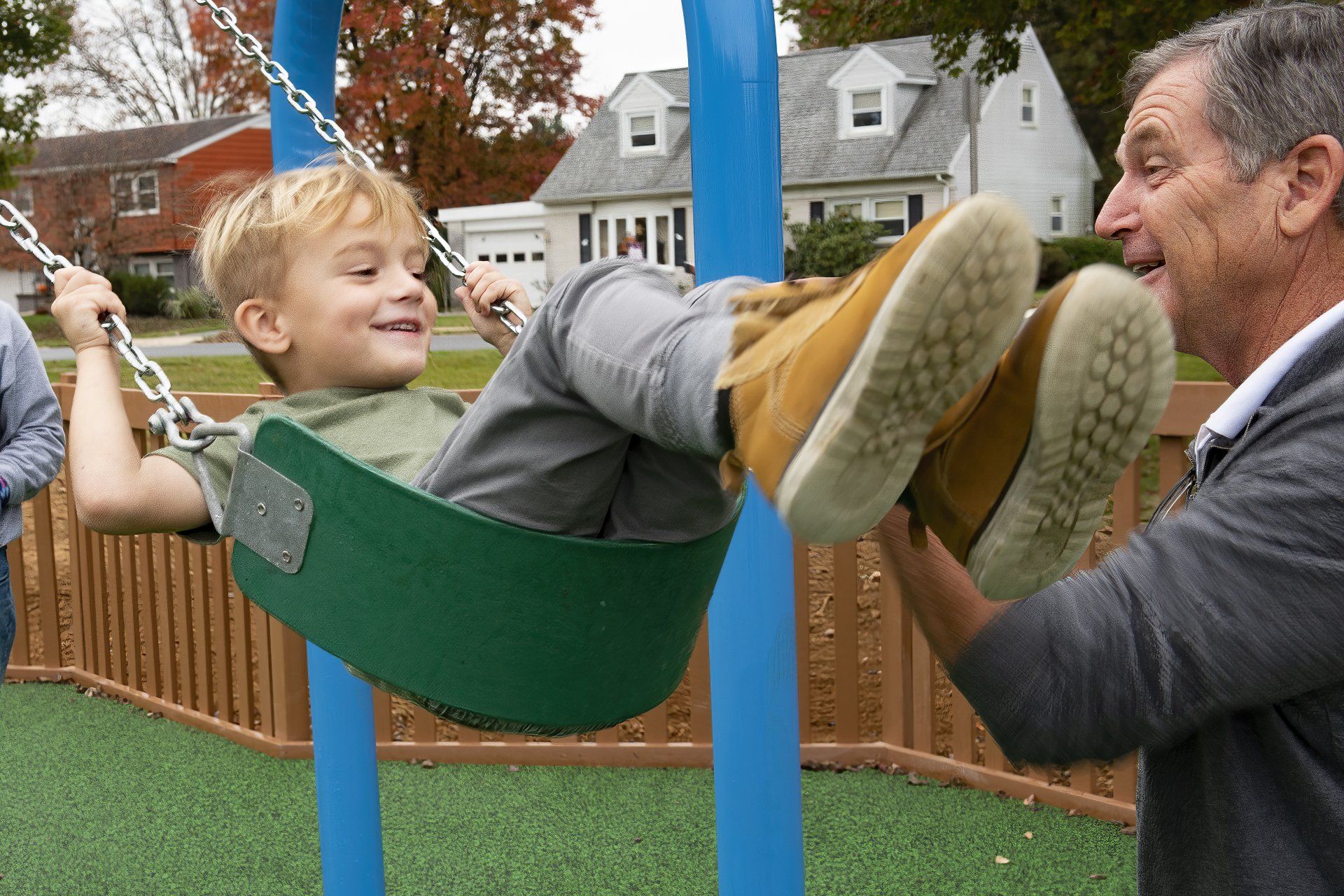 Boy on swing smiling, being pushed by a man at a playground.
