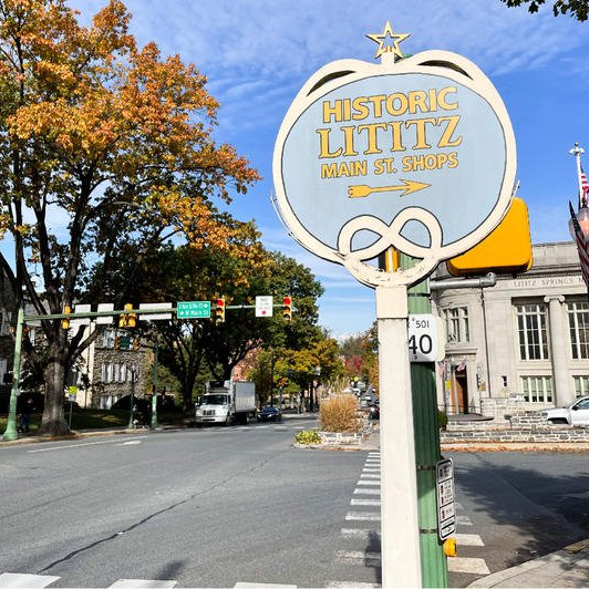 Sign for Historic Lititz, PA, with a pretzel design, at a street intersection on a sunny day.